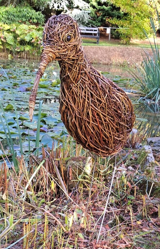 low curlew sculpture standing by a pind 
